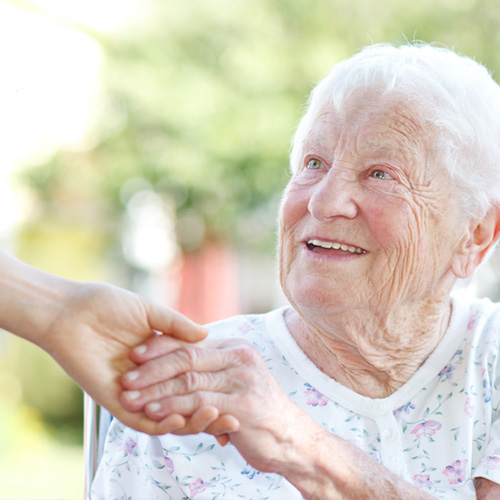 Seniorin lächelt und hält Hand vom Pflegeperson
